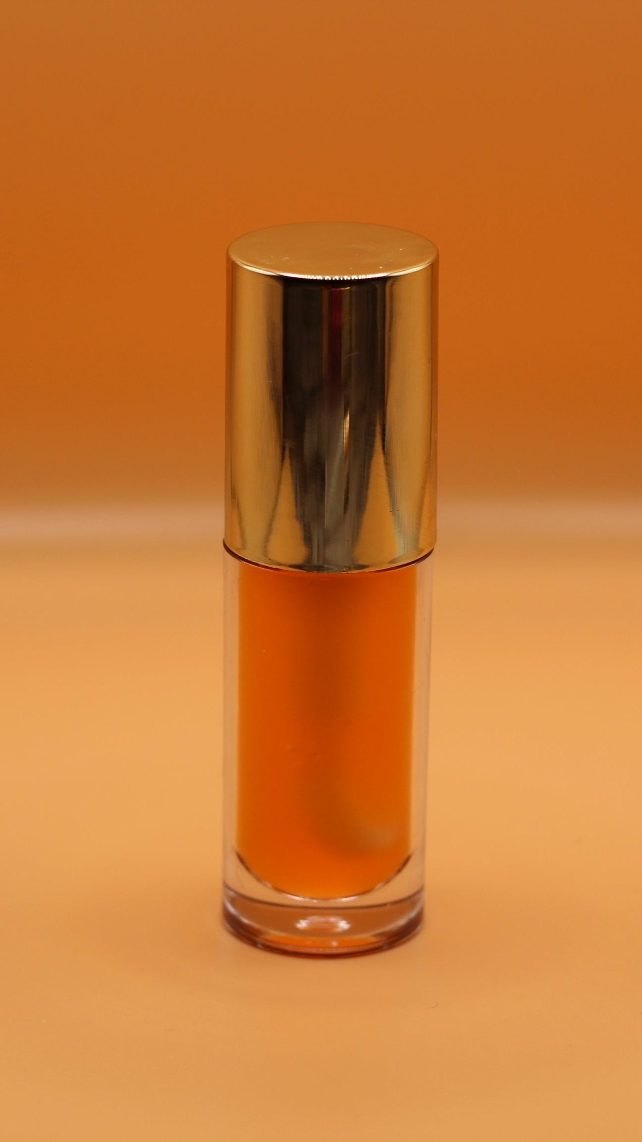 Soft yellow-orange tinted vegan lip oil with a tropical pineapple and peach scent, offering glossy hydration in a non-sticky formula.